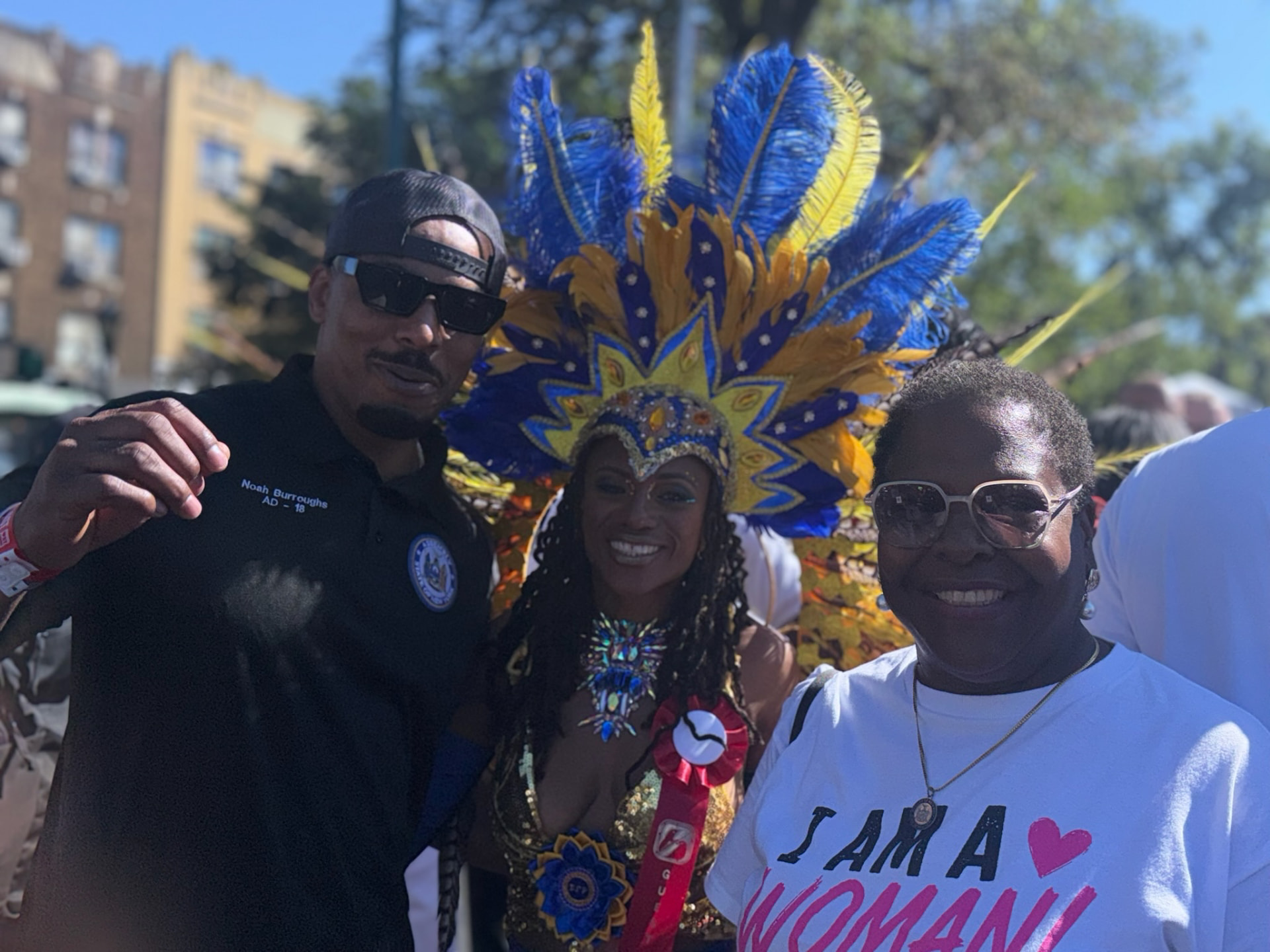 Three people together outdoors beside a blue and yellow feathered headdress